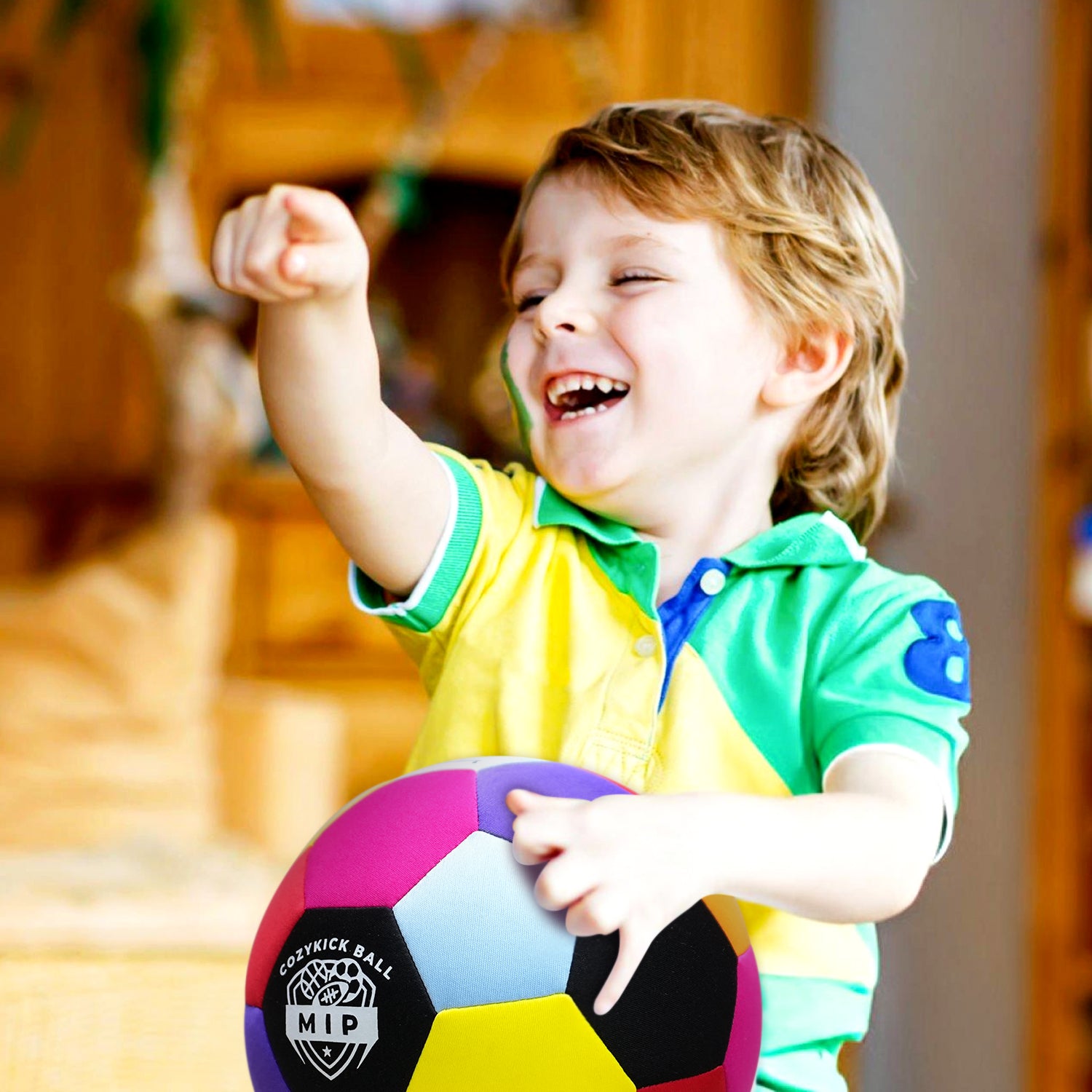 Colorful rubber kickball being held by a smiling child in a green and blue polo shirt.