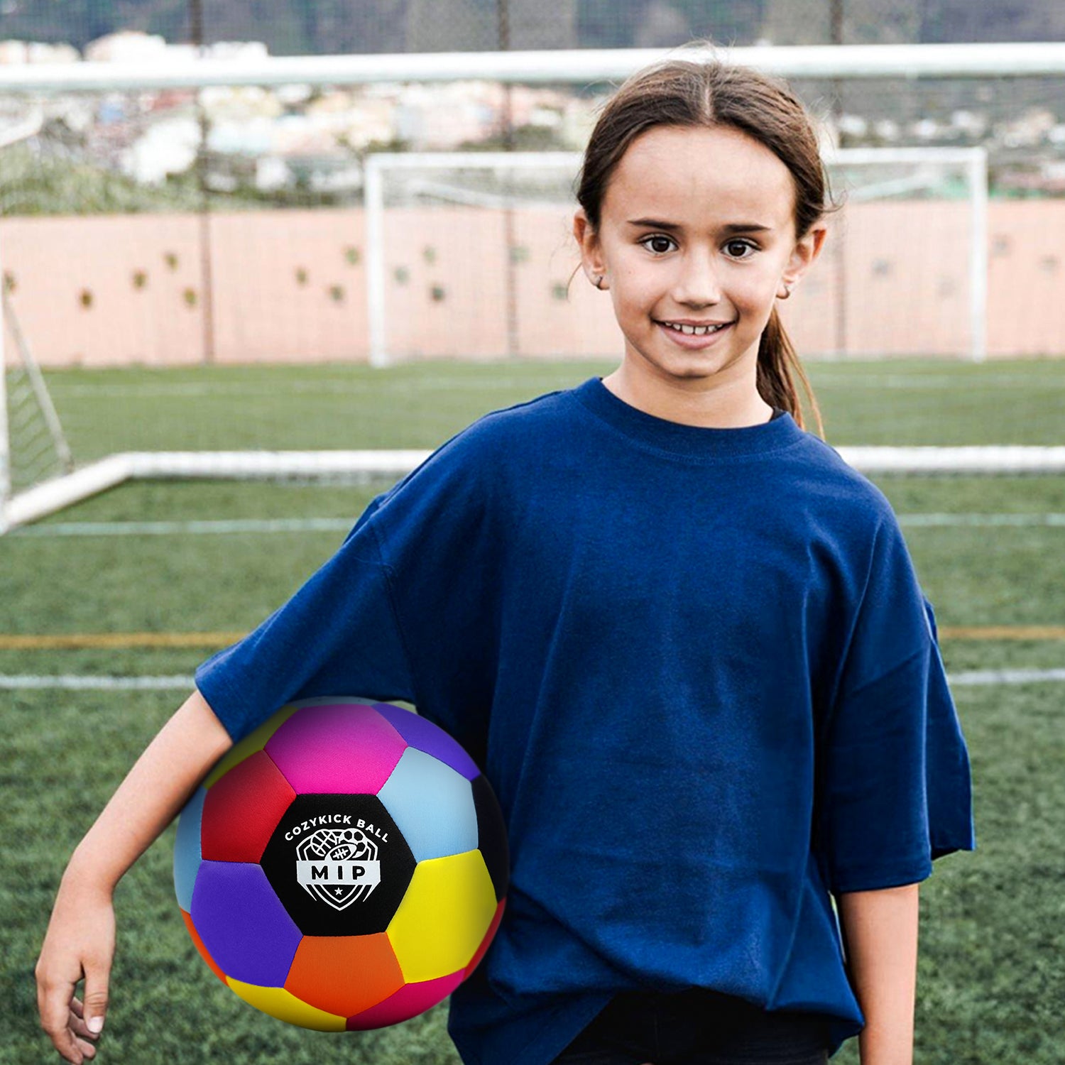 Blue oversized t-shirt worn by a girl holding a multicolored soccer ball on a grassy field.