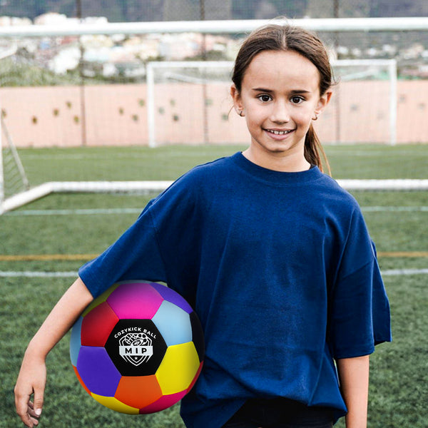 Blue oversized t-shirt worn by a girl holding a multicolored soccer ball on a grassy field.