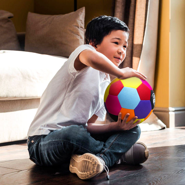 Colorful soccer ball held by a young boy sitting on the floor, wearing a white shirt and jeans.