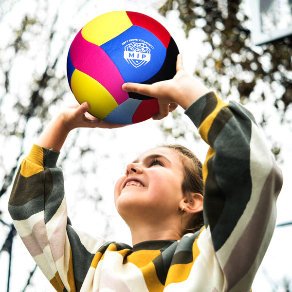 Multi-colored volleyball featuring MVP logo, held by girl wearing a striped sweater outdoors.
